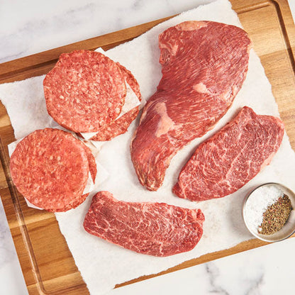 Cutting board with raw, uncooked Wagyu Burgers, American Wagyu Tri-tip and 2 American Wagyu Steaks