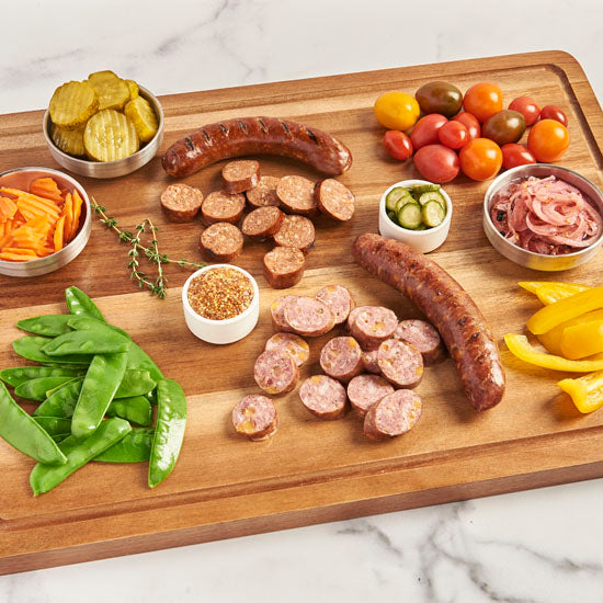 Elk and Bison sausages on a cutting board, cooked, cut up and ready to be eaten.  Surrounded by vegetables also ready to be eaten.