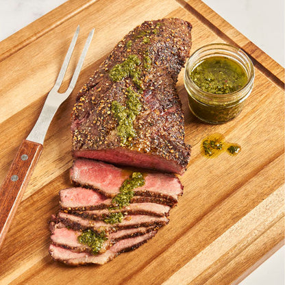 Prepared tri-tip steak with chimichurri on a cutting board ready to be eaten.