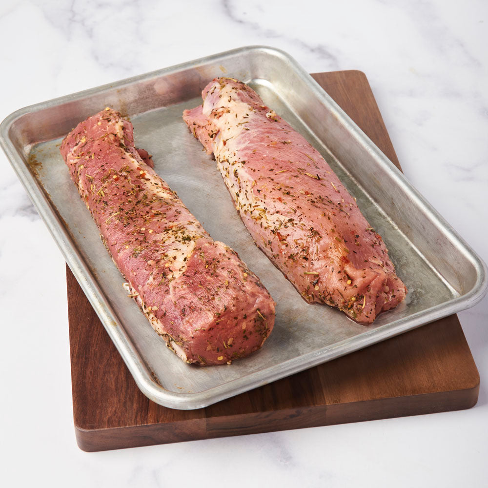 2 raw herb rubbed pork tenderloins in a sheet pan ready to be cooked.