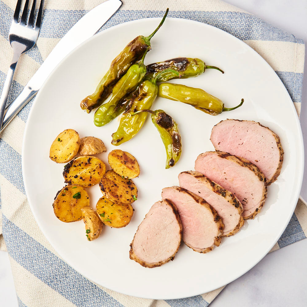 Sliced and cooked herb rubbed pork tenderloin on a plate with veggies ready to be eaten.