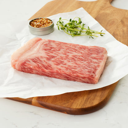 Raw A5 Japanese Wagyu 5 oz New York Strip on a cutting board ready to be cooked.